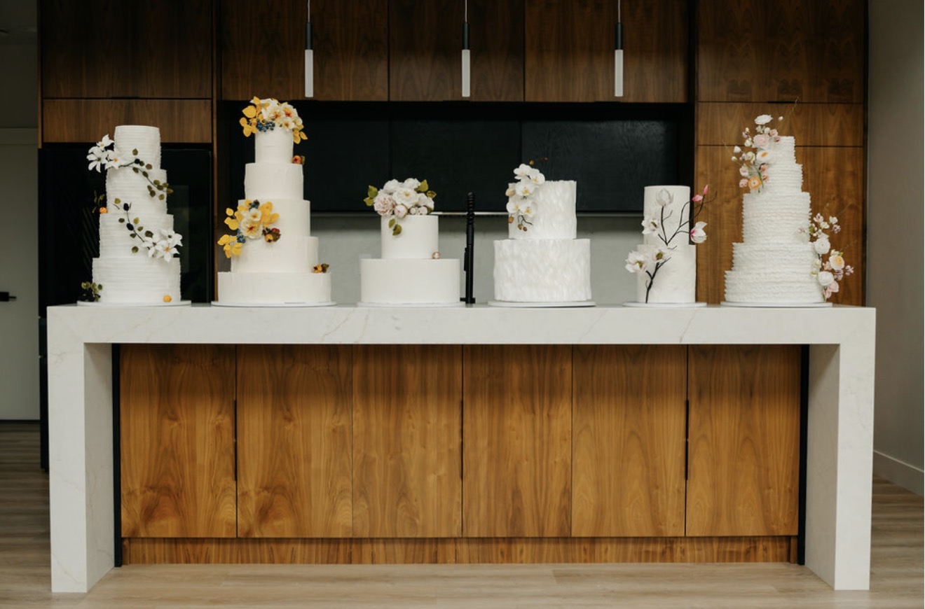 A lineup of six finished wedding cakes with sugar flowers displayed on a marble counter in the studio