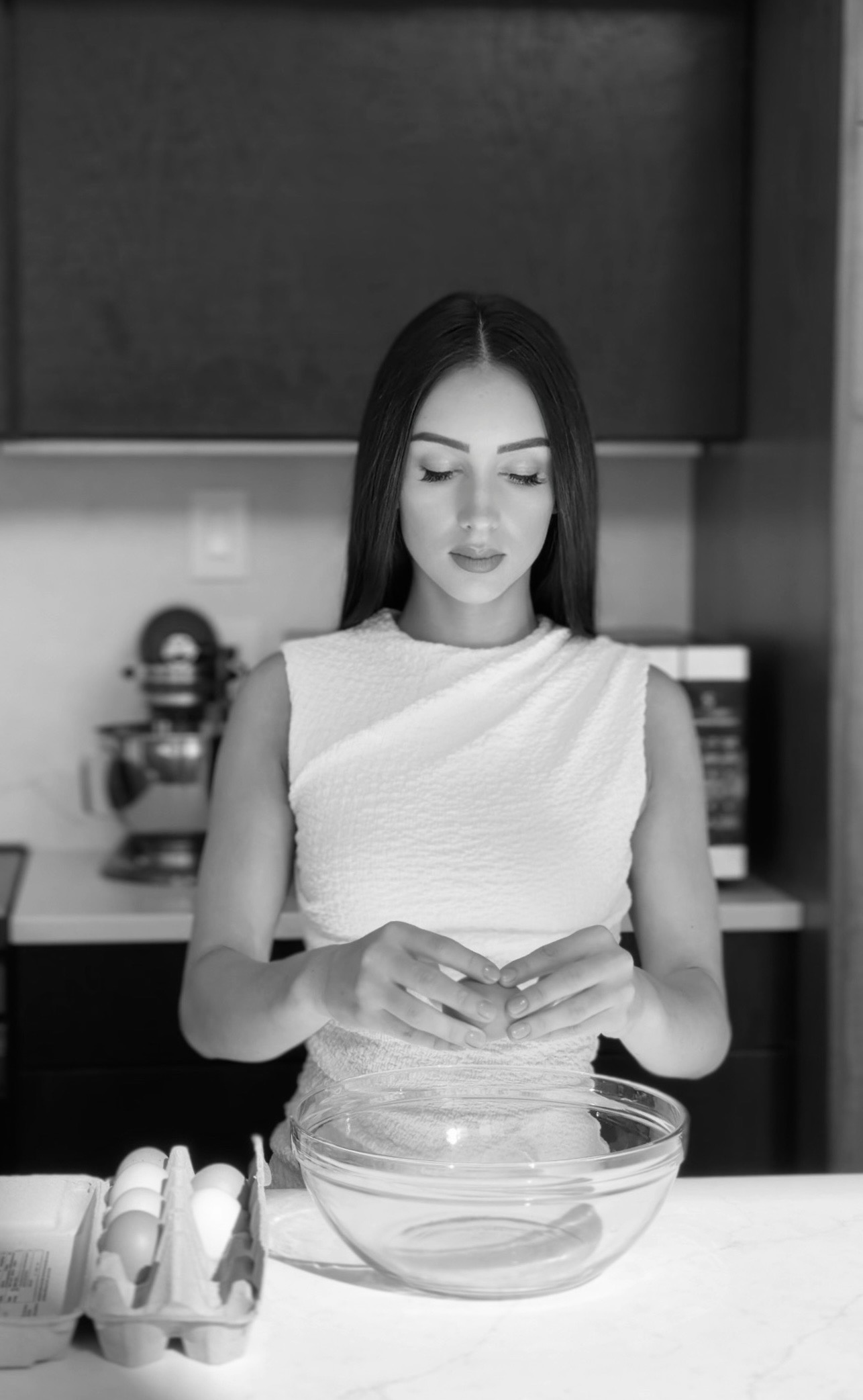 Black and white portrait of Magdalena cracking eggs into a glass bowl in her kitchen