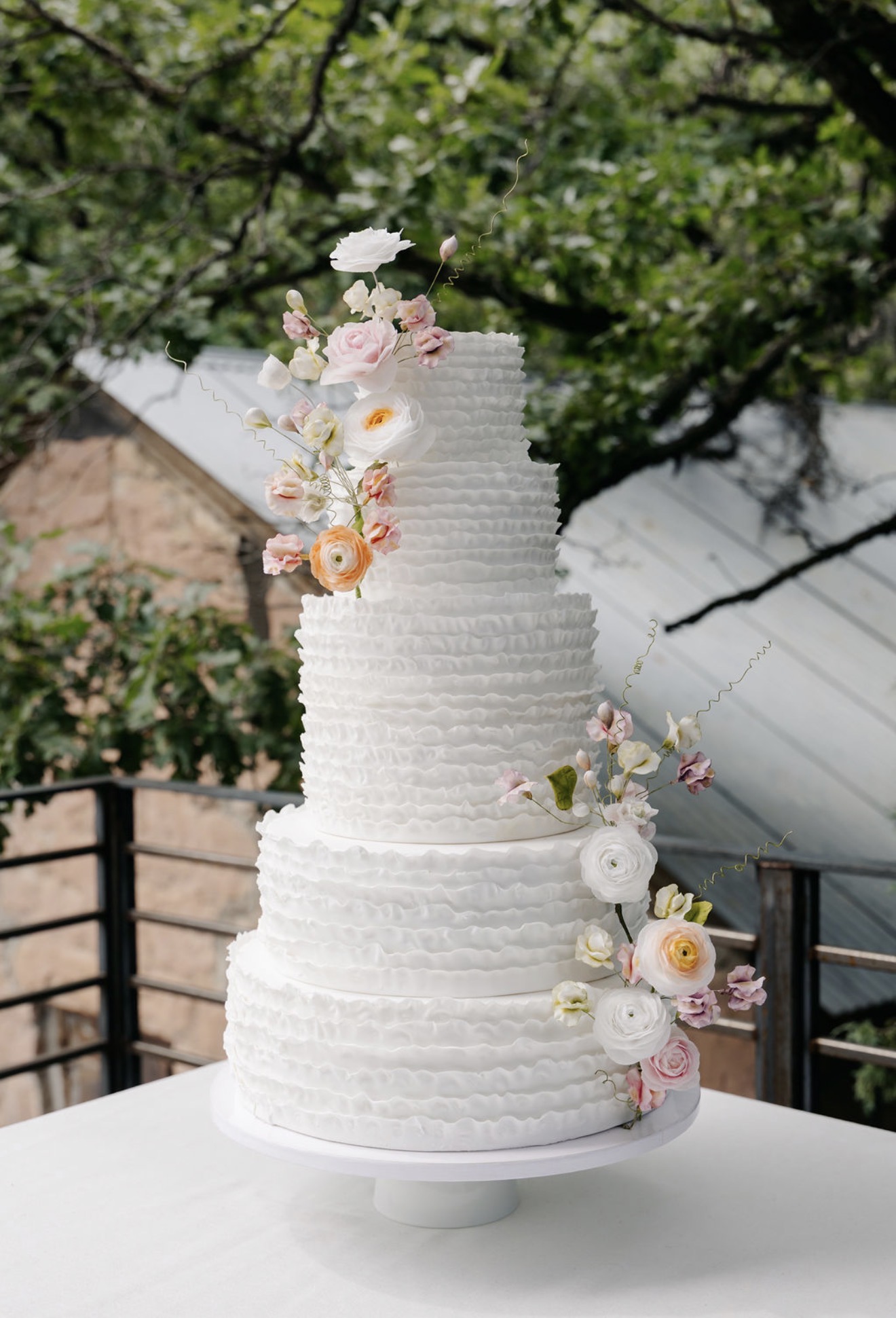 Five-tier ruffled wedding cake with pastel sugar ranunculus and sweet peas
