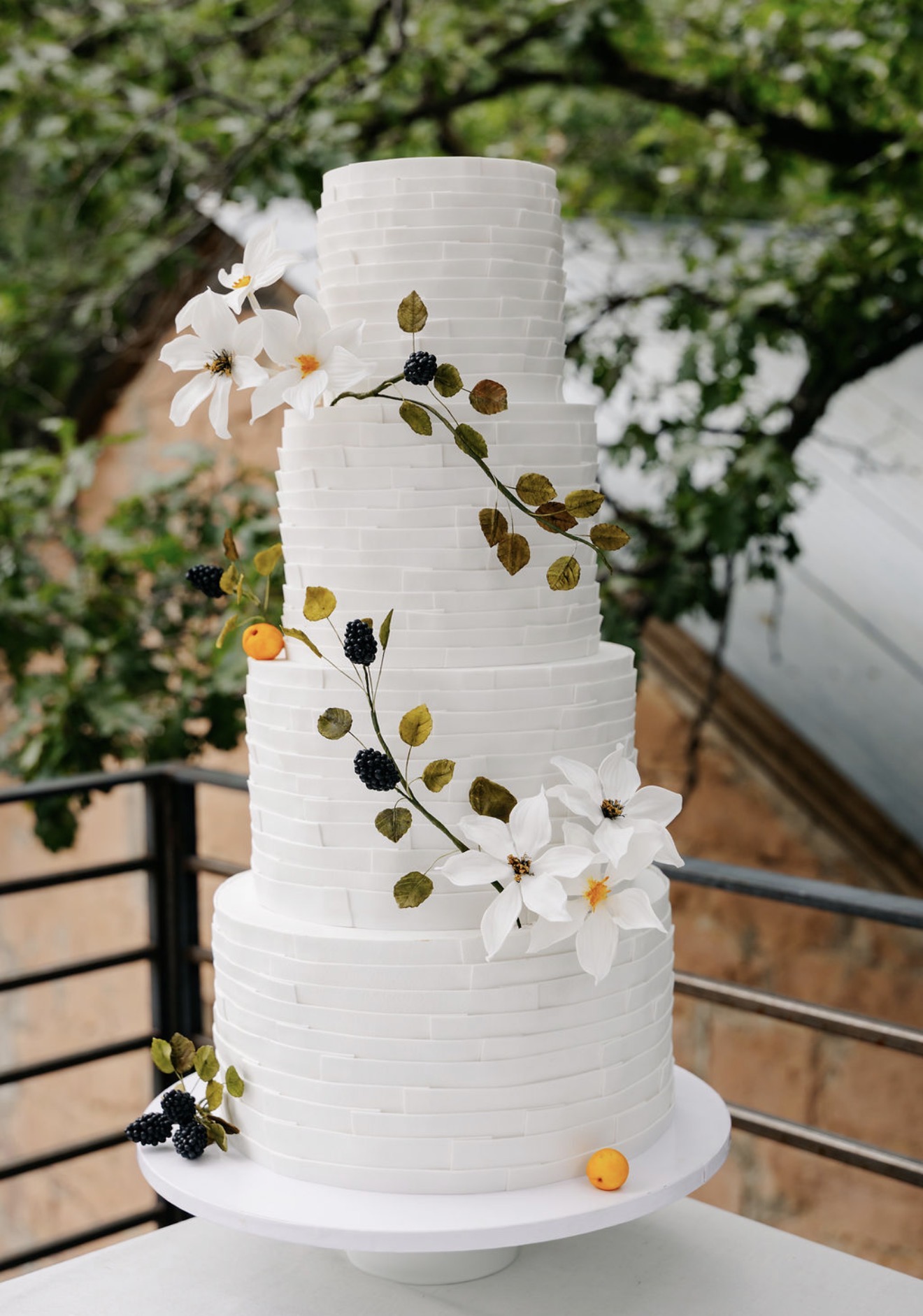 Four-tier ribbon-textured wedding cake with sugar clematis, blackberries, and apricots