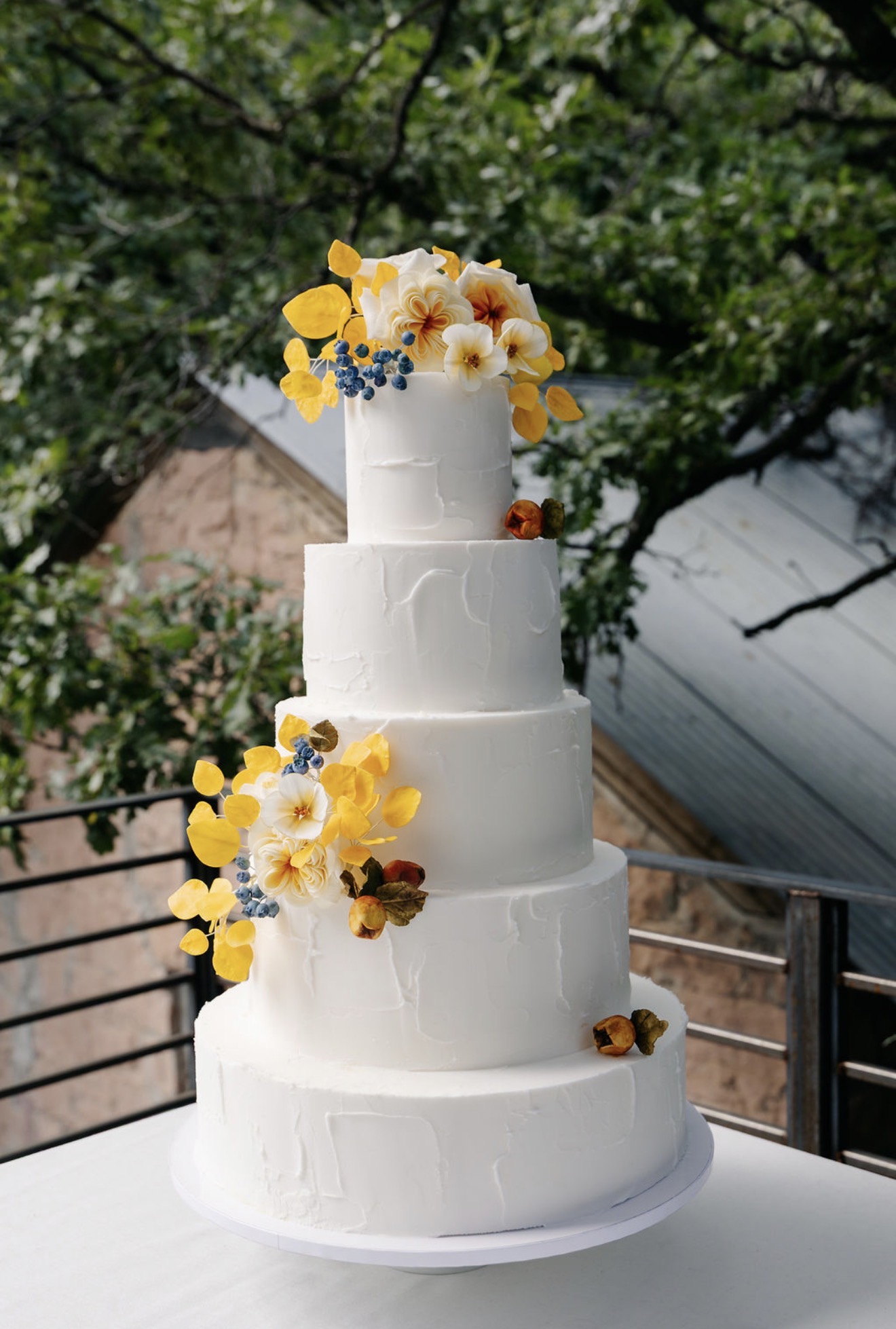 Five-tier textured wedding cake with golden sugar eucalyptus, blueberries, and garden roses