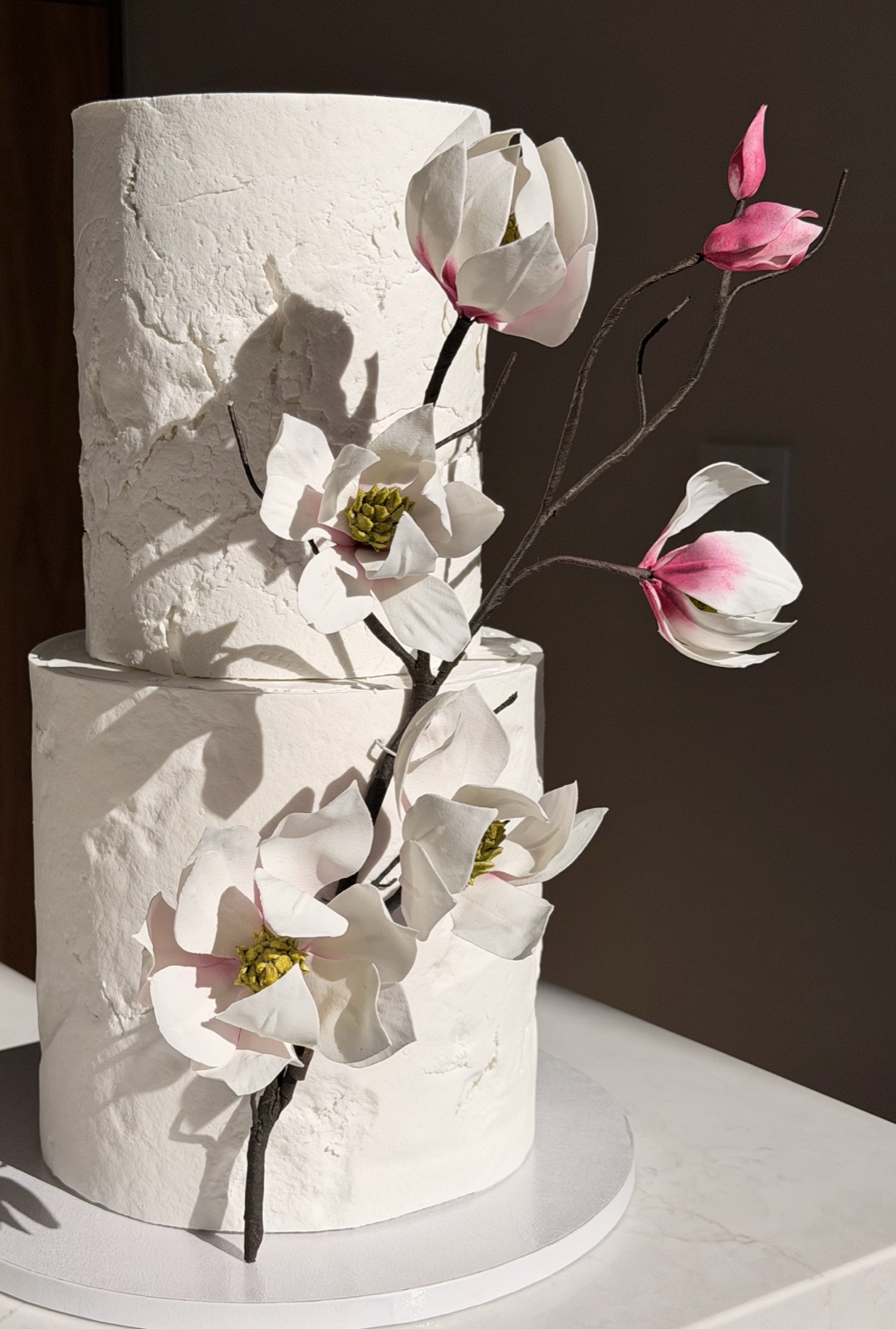 Textured white two-tier wedding cake with handcrafted sugar magnolia flowers on a branch