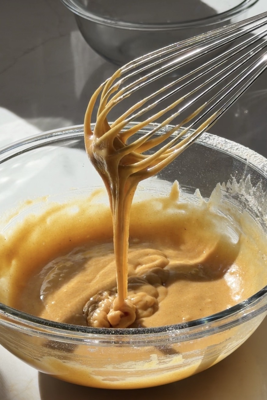 Cake batter being whisked in a glass bowl, catching natural light