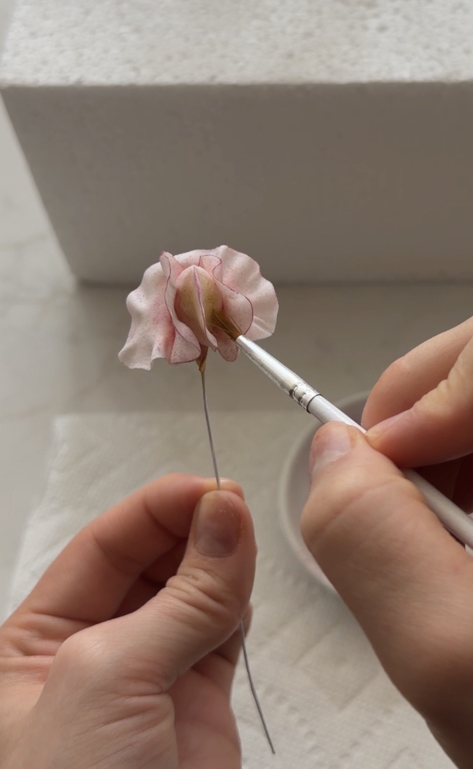 Hand-painting fine pink detail onto a sugar flower petal with a small brush
